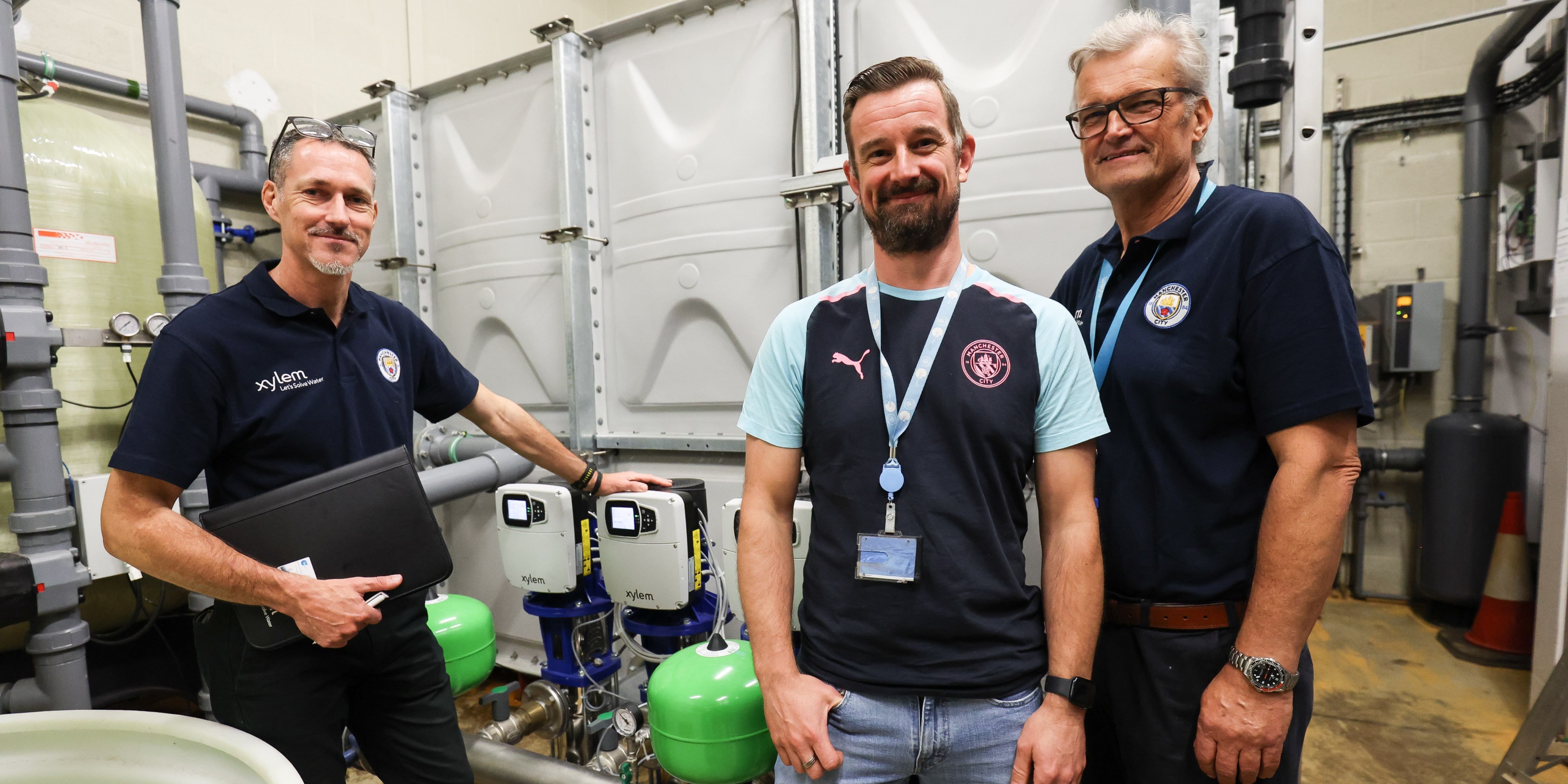 Xylem sales representatives and Manchester City maintenance operator pose in front of Hydrovar X water pump controller 